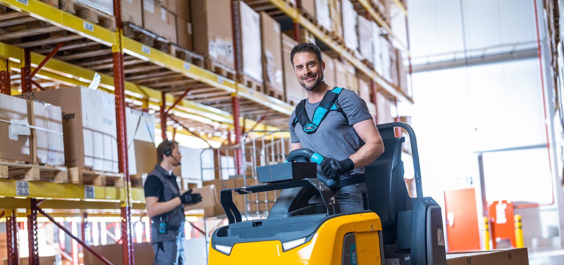 Several warehouse employees stand between storage racks and present different warehouse equipment such as Lydia VoiceWear, headsets, scanners and mobile devices that work with Lydia Voice.